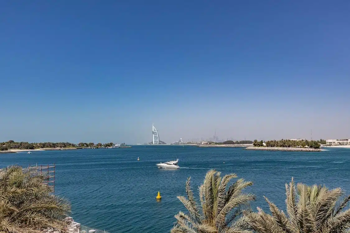 Free Breathtaking view of the Burj Al Arab from Dubai's coastline featuring serene waters and palm trees. Stock Photo