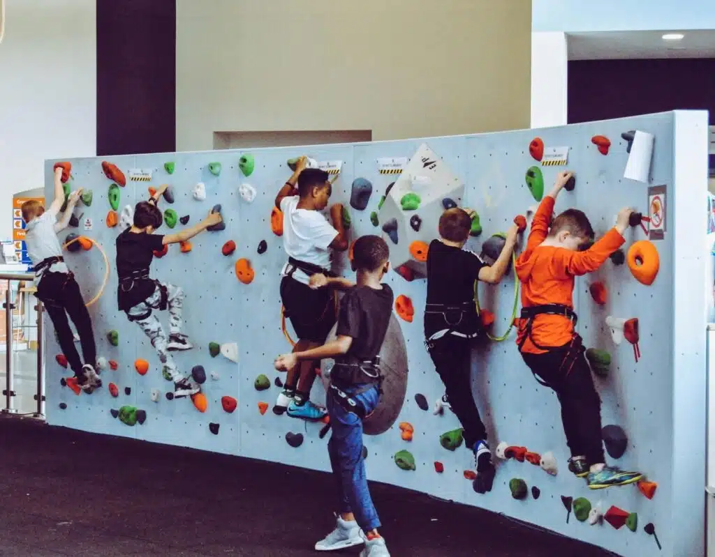 A group of kids climbing on a rock wall Description automatically generated