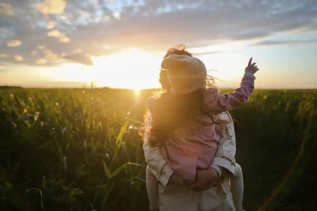 Free A mother and daughter embrace and point at the sunset in a grassy field. Stock Photo