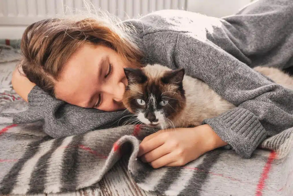 Woman lying on a bed cuddling with an emotional support cat.