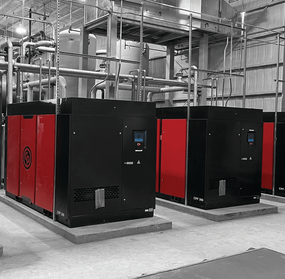Large industrial air compressors in a factory setting, showing multiple high-capacity units used for heavy-duty commercial applications