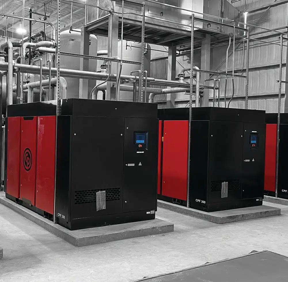 Large industrial air compressors in a factory setting, showing multiple high-capacity units used for heavy-duty commercial applications
