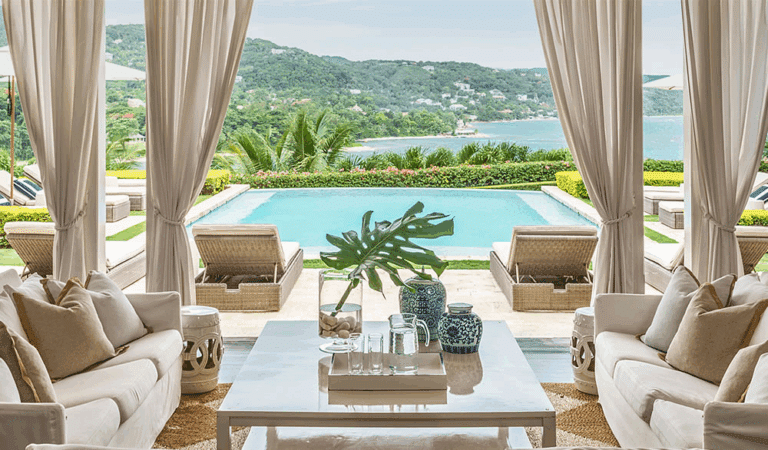 Luxury outdoor chaise lounges with powder-coated frames and neutral cushions on a teak deck, surrounded by tropical plants, ideal for warm-climate hotel patios.