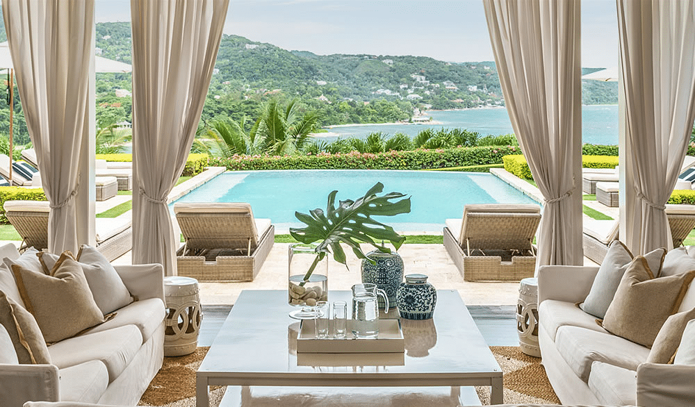 Luxury outdoor chaise lounges with powder-coated frames and neutral cushions on a teak deck, surrounded by tropical plants, ideal for warm-climate hotel patios.