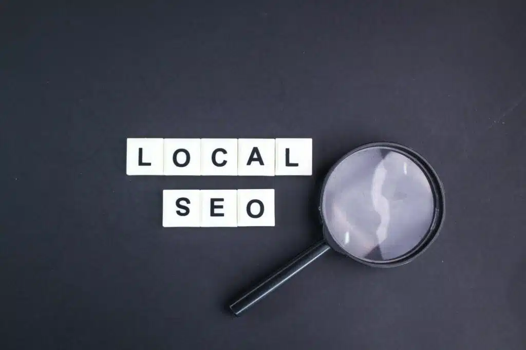 Magnifying glass next to letter tiles spelling "Local SEO" on a black background, representing keyword research and visibility for local SEO services.