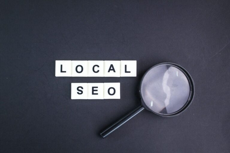 Magnifying glass next to letter tiles spelling "Local SEO" on a black background, representing keyword research and visibility for local SEO services.