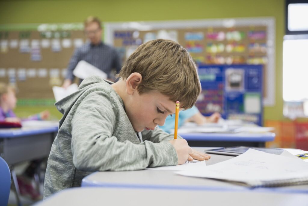 Focused elementary student writing at desk in classroom