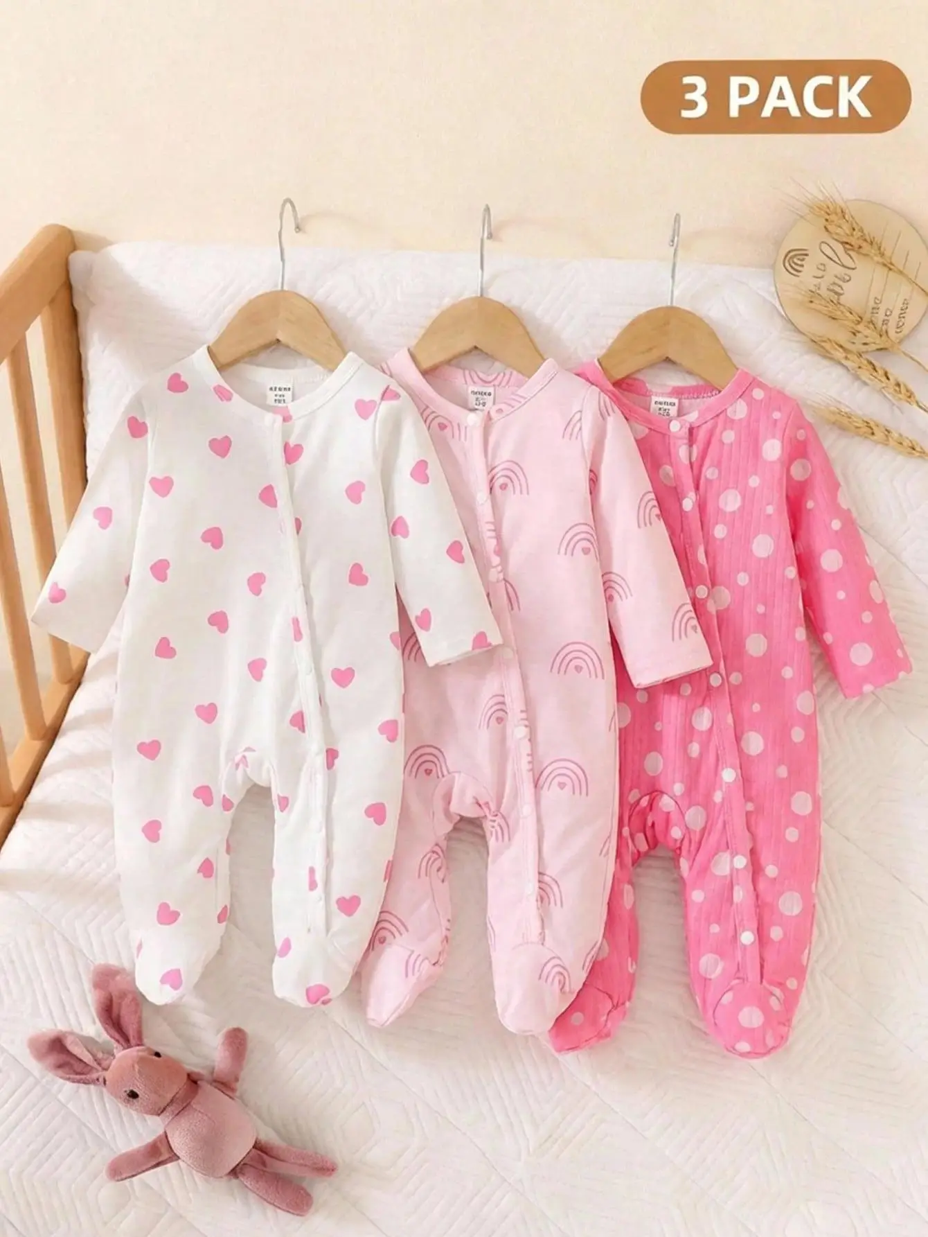 Three baby onesies with heart, rainbow, and polka dot patterns on crib rails
