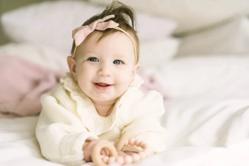 Baby with pink bow headband lying on white bedding in soft natural light