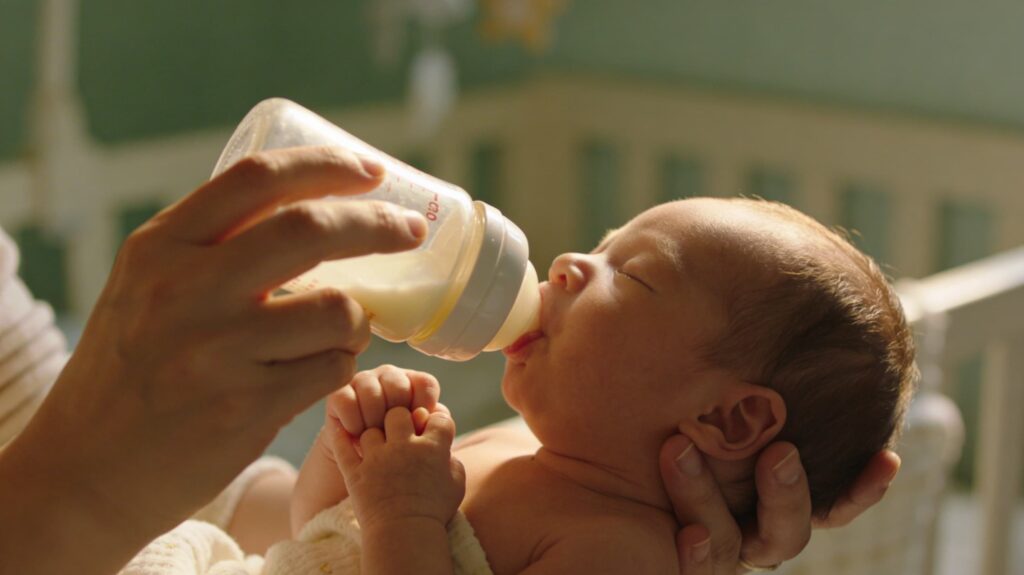 Caregiver feeding a newborn with a bottle while supporting the baby’s head, demonstrating paced bottle feeding technique.
