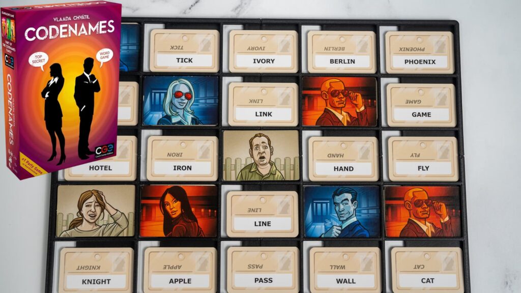 Codenames board game setup showing a grid of word cards and agent tiles, with the game box displayed beside the board