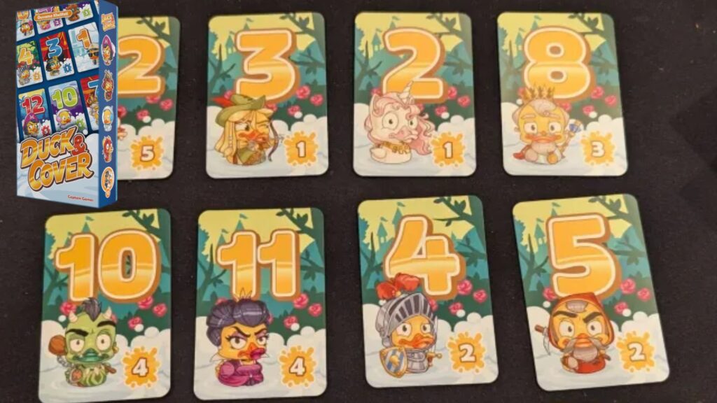 Duck and Cover card game layout showing numbered character cards arranged on a table, with the game box displayed in the corner