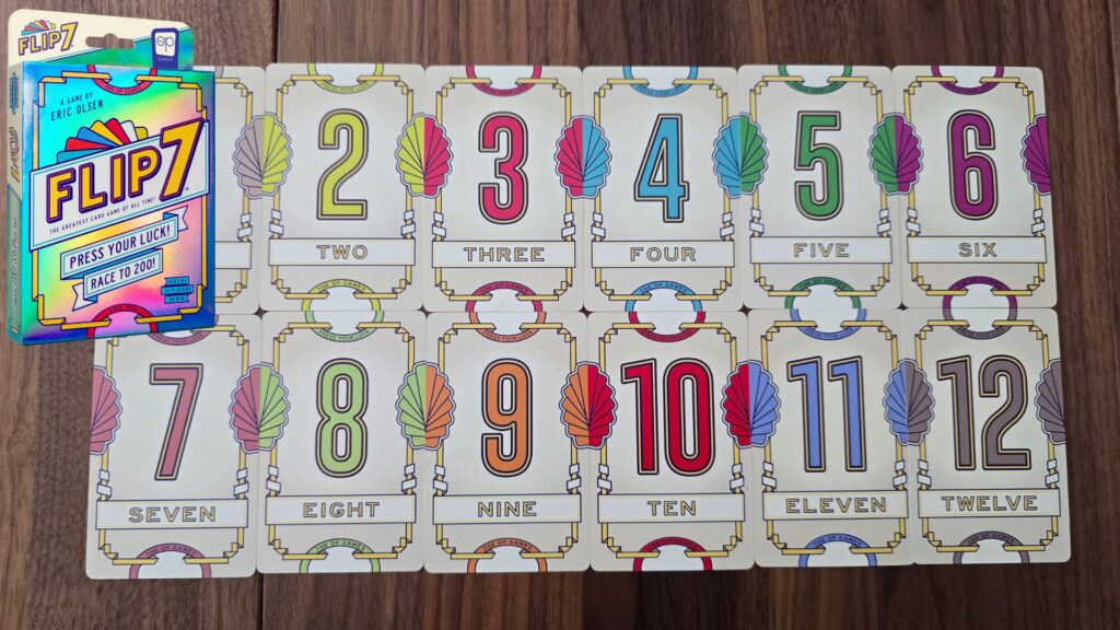 Flip 7 card game display showing numbered cards from 0 to 12 arranged in rows on a wooden table, with the colorful game box visible in the corner