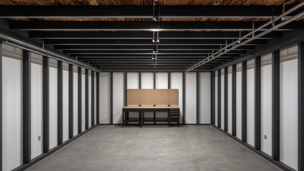 Modern unfinished basement with drywall panels installed between exposed joists, featuring a clean grid ceiling, metal framing, and a simple workbench along the back wall