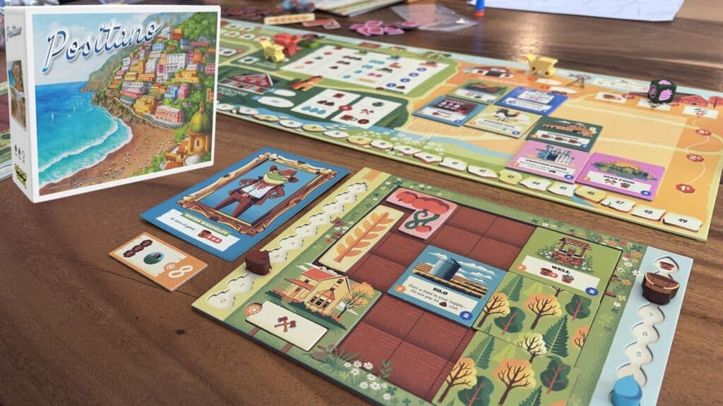 Positano board game setup on a wooden table, featuring a colorful game board, player boards with cards and tokens, and the illustrated game box showing a coastal town scene