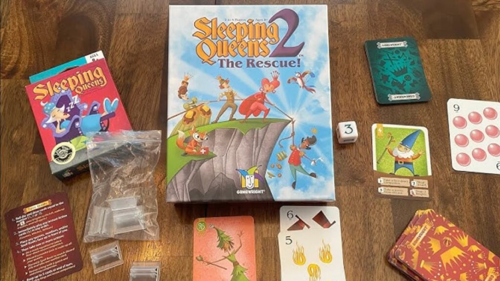 Sleeping Queens 2 The Rescue board game components arranged on a wooden table, including the main game box, cards, dice, player pieces, and a smaller Sleeping Queens game box