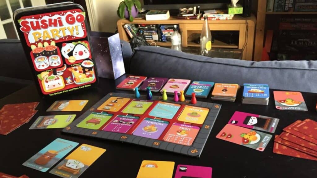 Sushi Go Party board game set up on a table with colorful cards, player pieces, and the game box displayed in the background