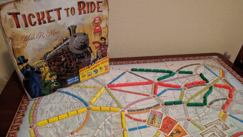 Ticket to Ride board game set up on a table with colorful train pieces placed across the map, and the game box displayed in the background