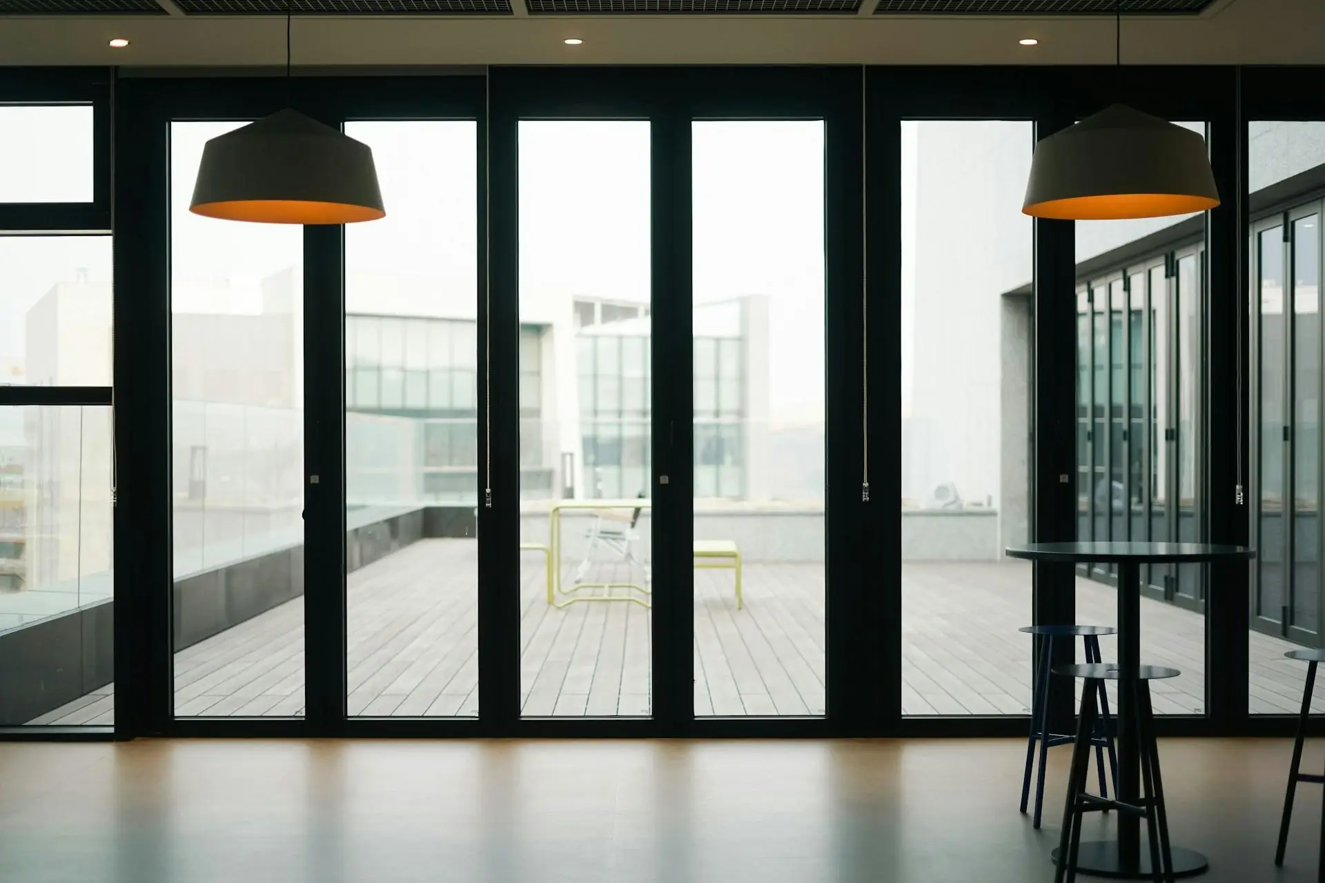 Large glass doors opening to terrace with outdoor seating, black stools, and pendant lighting indoors
