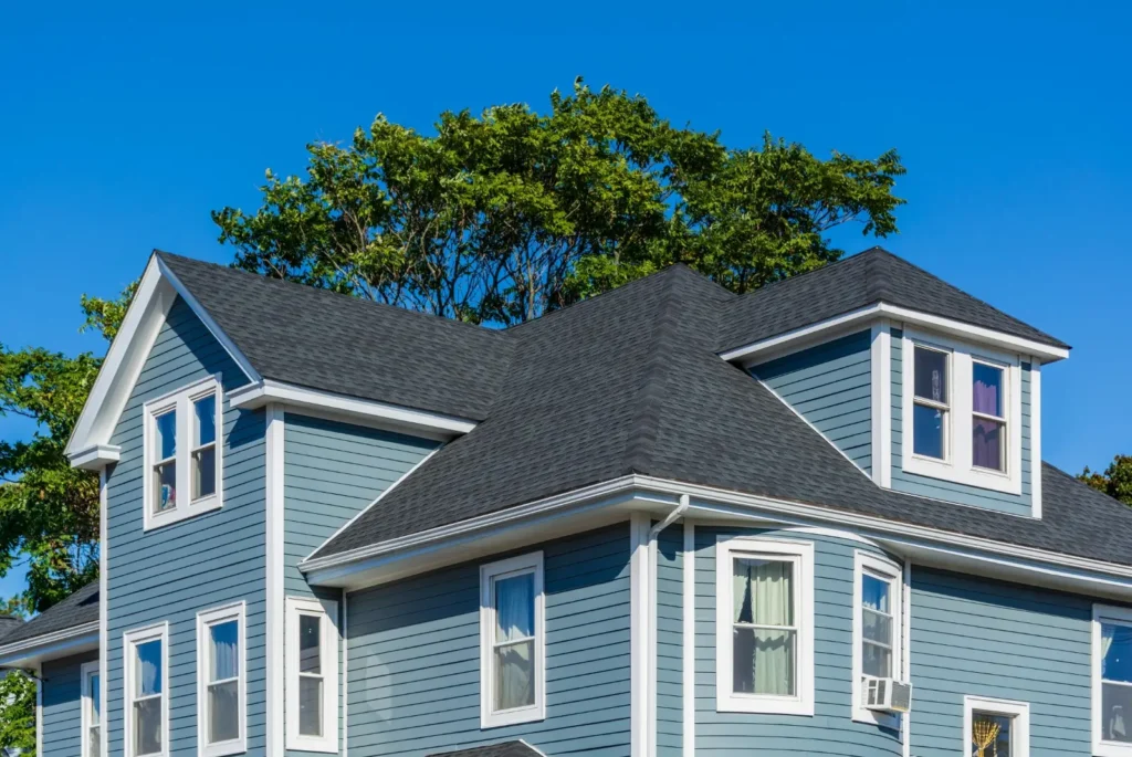 Blue wooden house exterior with gabled roof against clear blue sky and green trees