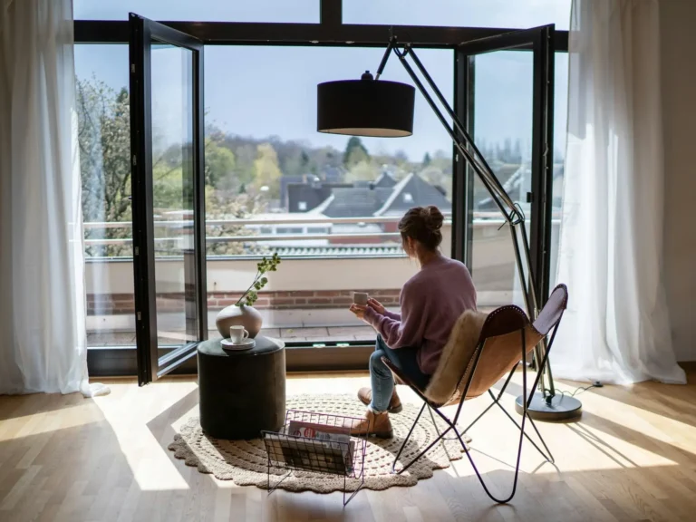 Woman sitting in cozy living room with large windows and a view of rooftops