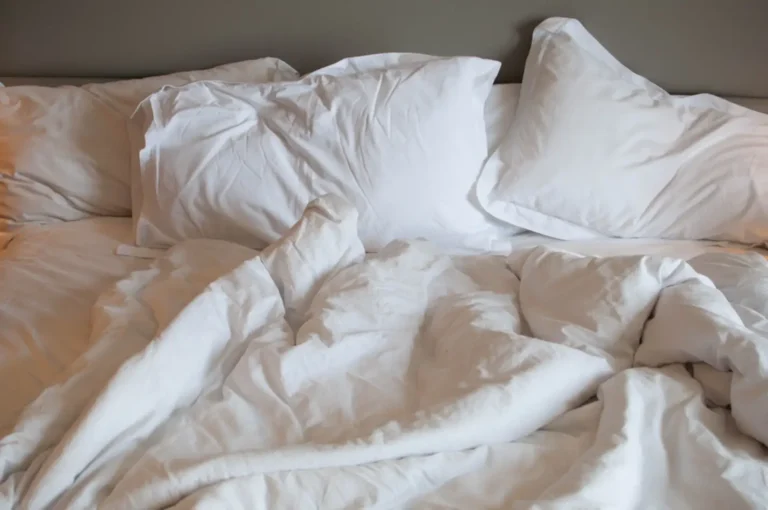 Wrinkled white bed sheets and pillows in a softly lit bedroom setting