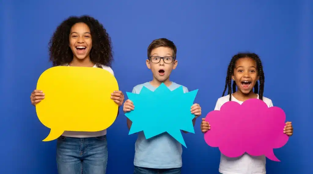 Three children smiling and holding colorful, empty speech bubbles against a blue background.