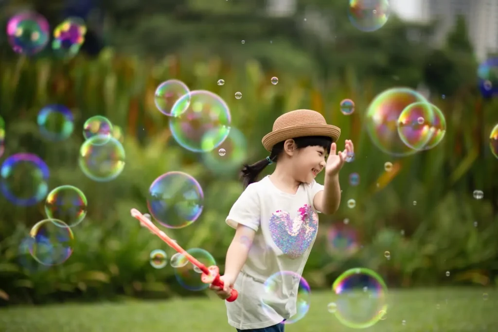 Child in straw hat playing with bubbles in green park