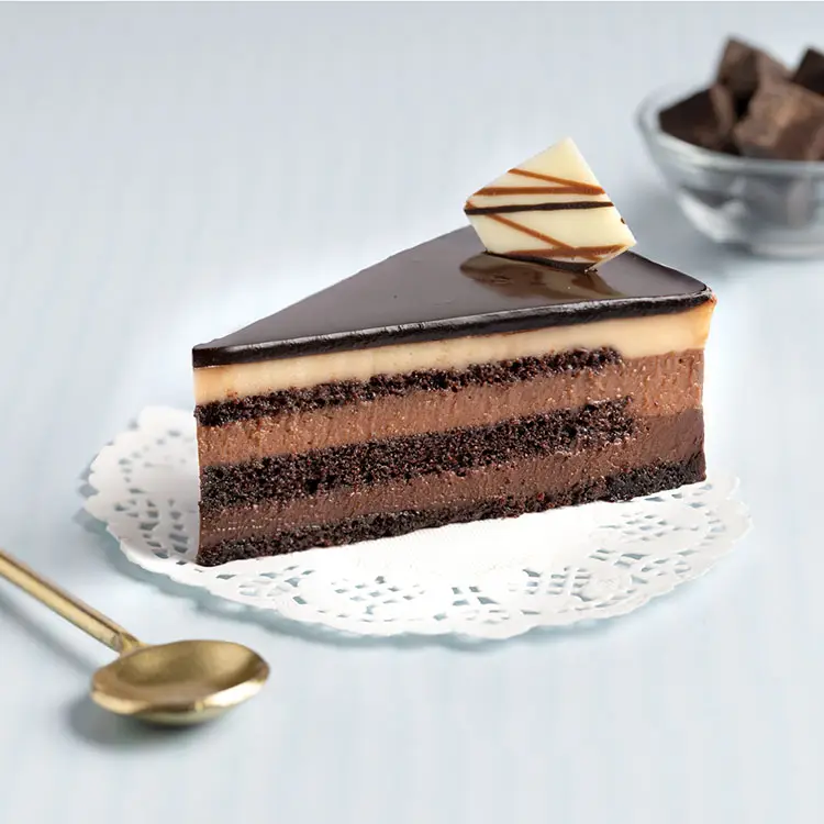 Chocolate mousse cake slice with layered ganache on doily beside gold spoon