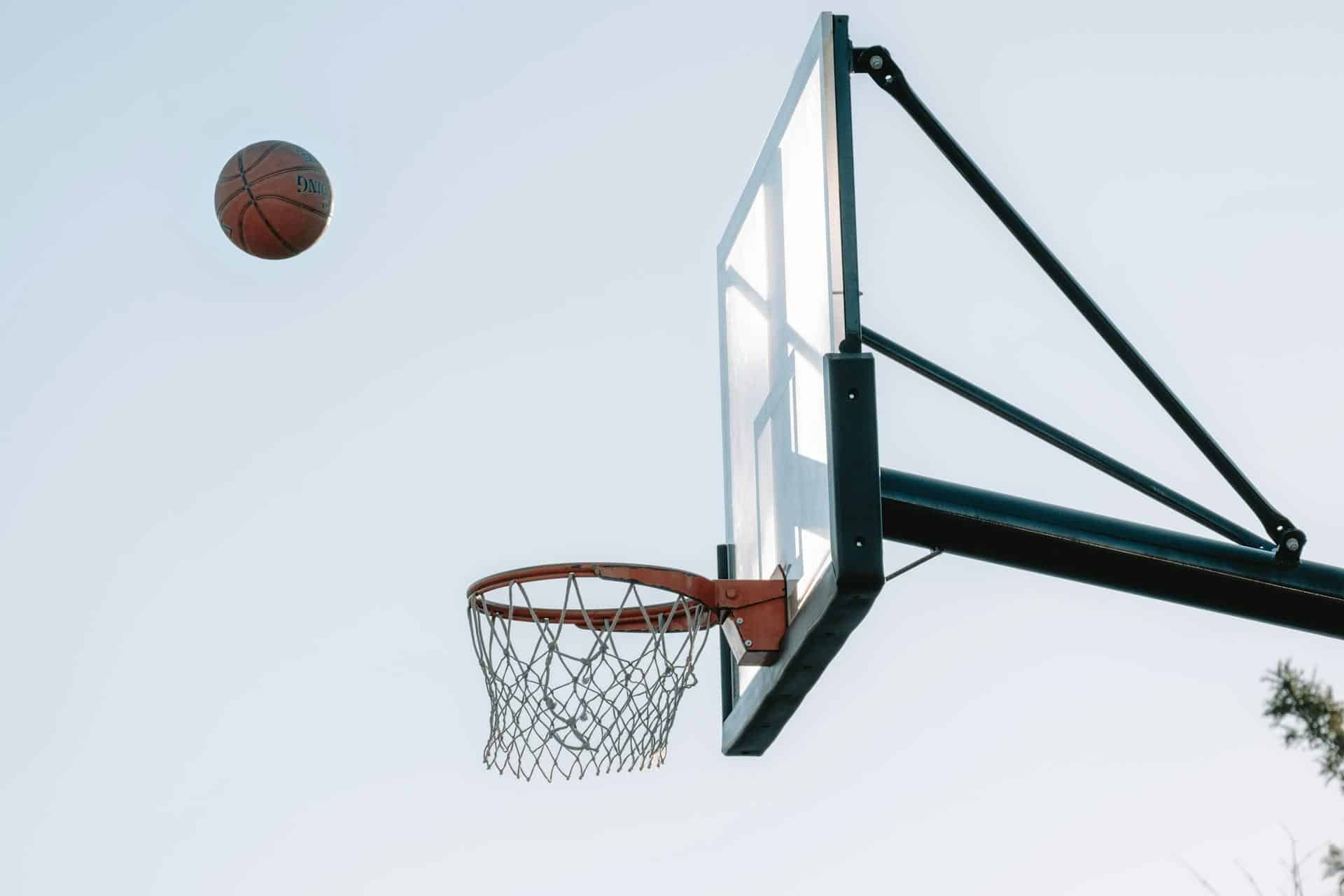 Basketball approaching hoop against clear blue sky in an outdoor setting